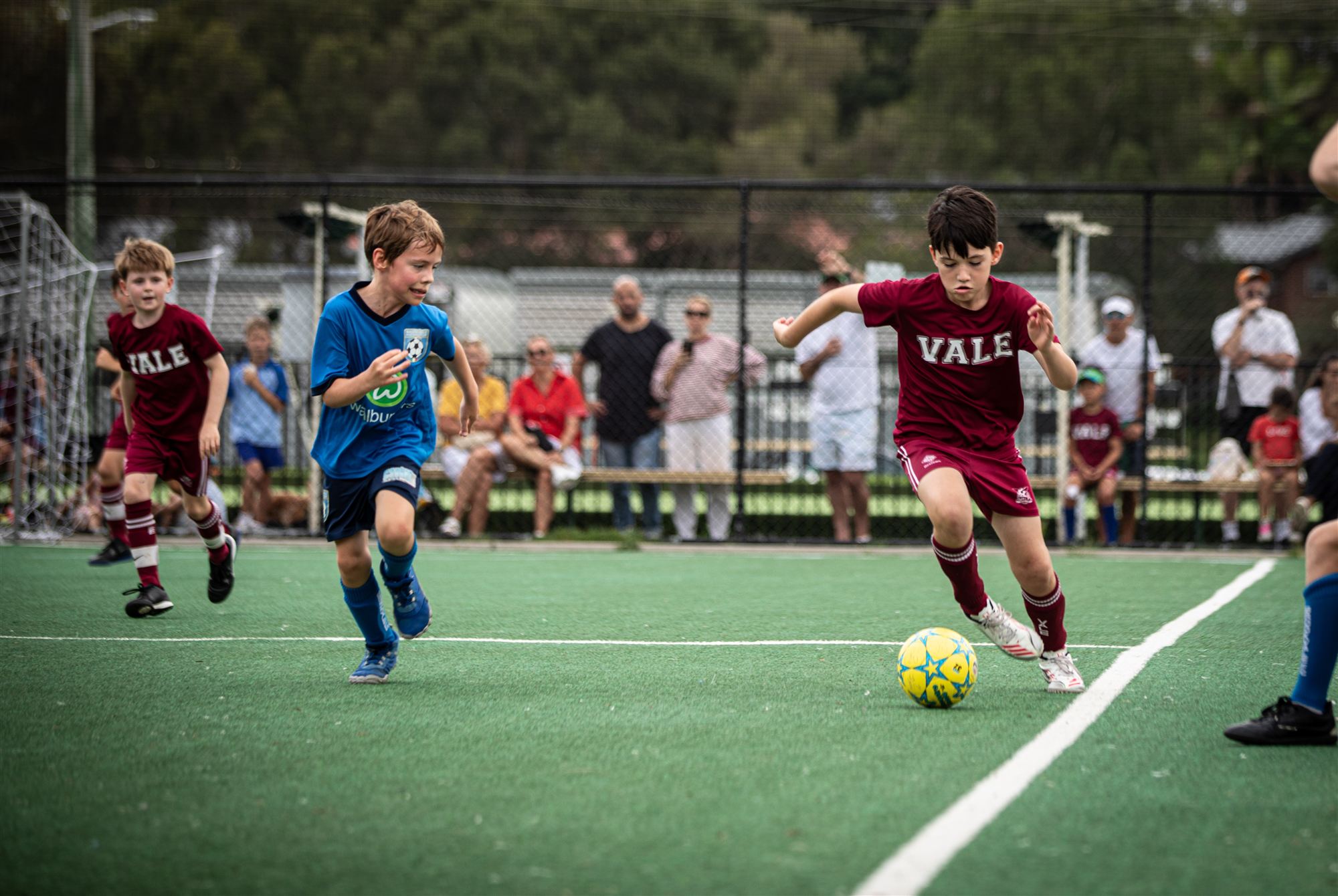 Vale player driving forward with the ball in front of a jacaranda tree in full bloom